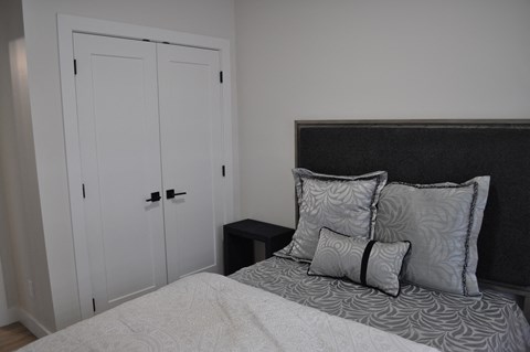 A bed with a white comforter and two pillows sits in a room with a white closet at The Laurent at Laurel Apartments, Edmonton, Alberta